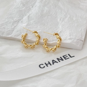 Irregular double C-shaped golden hoop earrings with textured finish on white stone surface