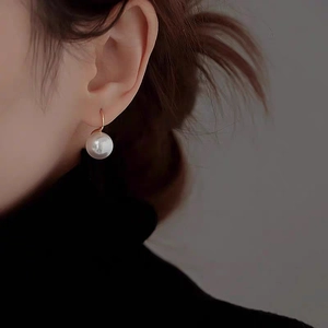 Elegant pearl drop earrings with round white pearls and gold hooks on a model