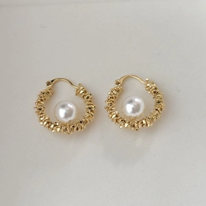 Macro shot of gold-plated hoop earrings featuring vintage textured metal and white pearl