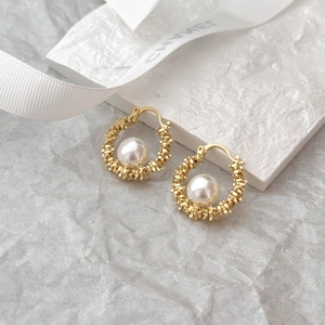 Elegant gold woven textured hoop earrings with pearl centers on a premium white display