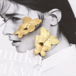 Golden double butterfly earrings with vintage metal texture on a fashion magazine background
