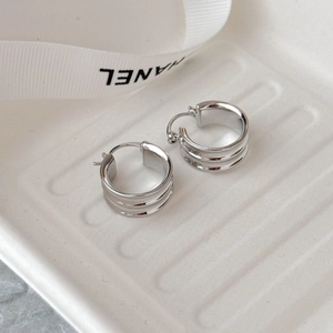 Vue macro de boucles d'oreilles créoles argentées à trois couches sur plateau blanc