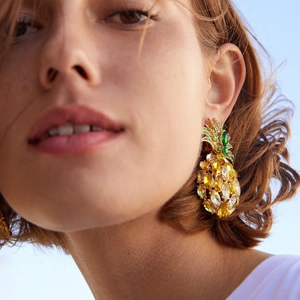 Sparkling pineapple stud earring with yellow and green crystals worn against a blue sky