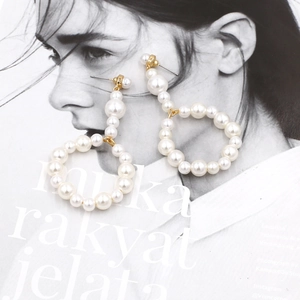 Close-up of oversized white pearl hoop earrings with gold metal studs and elegant luster
