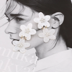 Exaggerated white acrylic floral earrings with pearl centers on fashion magazine background