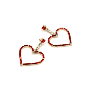 Close-up of heart-shaped gold drop earrings with red crystals and diamond accents