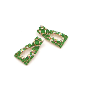 Macro detail of geometric gold earrings with vibrant green crystals and AB rhinestones