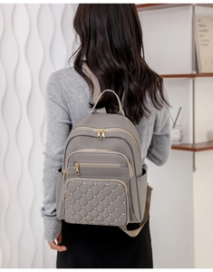 Close-up of stylish gray oxford backpack with quilted pattern and gold studs on a model