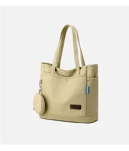 Detail of beige canvas tote bag showing metal buckle, side logo, and small round coin purse