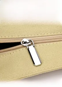 Close-up of smooth silver metal zipper and durable canvas texture on a beige handbag