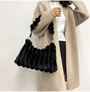Detail of black faux fur shoulder bag with vertical pleats and decorative fur ball strap
