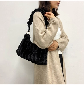 Detail of black faux fur shoulder bag featuring ruffled texture and plush ball strap
