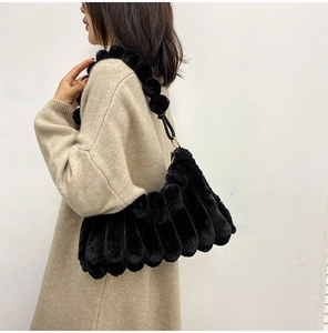 Detail of black faux fur shoulder bag featuring vertical pleats and plush ball strap