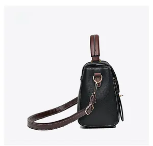 Détail du sac en cuir noir avec bandoulière marron contrastée et boucles dorées