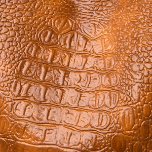 Close-up of tan faux leather with embossed crocodile pattern and glossy finish