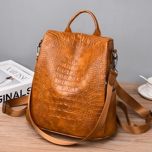 Detailed view of brown crocodile texture leather backpack with top handle on a wood surface