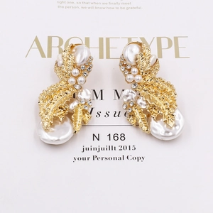 Detail of golden leaf earrings with baroque pearls and sparkling crystals on a white paper