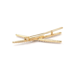 Detail of a golden criss-cross hair clip featuring a row of elegant white pearls on top