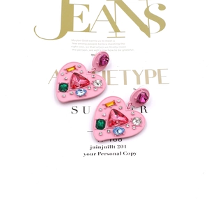Close-up of pink heart earrings with colorful rhinestones on a magazine background