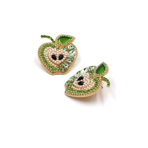 Macro view of green crystal apple earrings with pearl inlay and golden metal finish