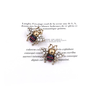 Vintage gold bee stud earrings with inlaid pearls and sparkling crystals on white paper