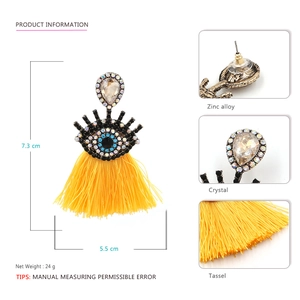 Detailed view of evil eye earrings with crystal inlays and yellow tassels on white backdrop