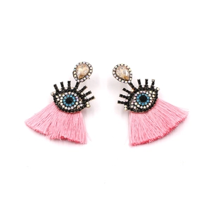 Macro detail of pink fringe earrings with crystal evil eye accent and teardrop gems