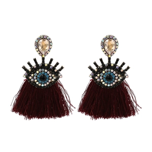 Macro shot of evil eye earrings featuring blue crystal inlay and deep red tassel details
