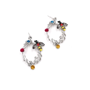 Dettaglio di orecchini ovali con api di cristallo colorate e rose rosse su metallo argento