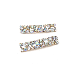 Detail of two rectangular gold hair clips with colorful rhinestones on a white background