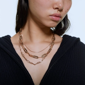 Collier doré à trois rangs avec maillons trombone, porté par un mannequin sur fond noir