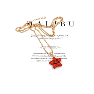 Golden bead necklace with a red sparkling star pendant featuring a black smiley face design