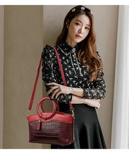 Détail du sac à main rouge à motif crocodile avec garniture dorée porté par un mannequin