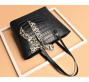 Close-up of black crocodile pattern tote bag with leopard print scarf and gold logo