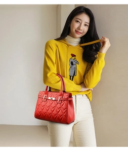 Detail of red heart-quilted leather handbag with gold metal clasp on a female model