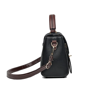 Sac à main en cuir noir avec bordure marron et bandoulière réglable sur fond blanc