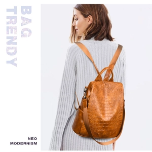 Detailed view of the crocodile pattern caramel backpack worn by a model on grey knitwear