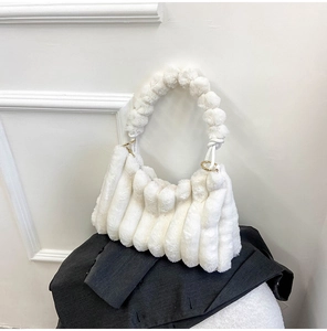 Detail of white pleated faux fur handbag featuring plush ball handle and gold hardware