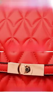 Detail view of red quilted leather texture and golden metal twist lock on a shoulder bag