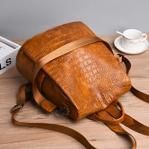 Detail view of brown crocodile pattern leather backpack on a wooden desk setup