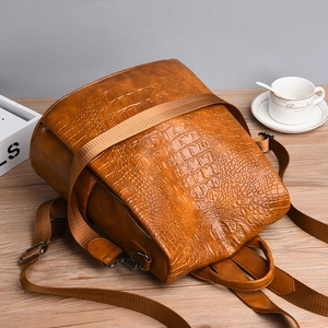 Detailed view of brown crocodile texture leather backpack on a wooden table with coffee cup