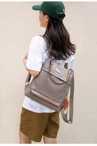 Outdoor shot of a woman carrying a grey-purple nylon backpack with leather straps and metal tag