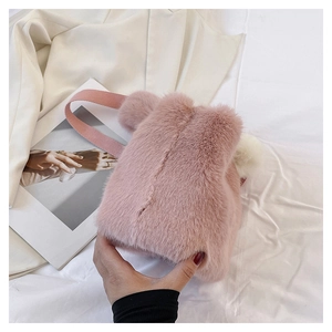 Detailed view of pink plush bucket bag with fuzzy white pom-pom and wide fabric strap