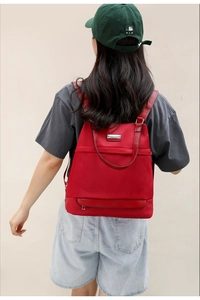 Side view of red oxford backpack with leather handles and metallic brand plaque on model
