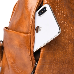 Detail of caramel leather backpack showing side zipper pocket holding a smartphone