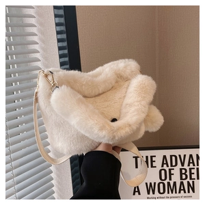 Detail of soft cream plush shoulder bag featuring gold hardware and fluffy pom pom charm