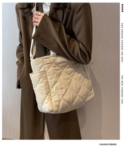Detail of beige quilted tote bag with diamond pattern and side pocket on a model