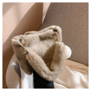 Detail of soft beige faux fur handbag featuring a golden buckle and white plush charm