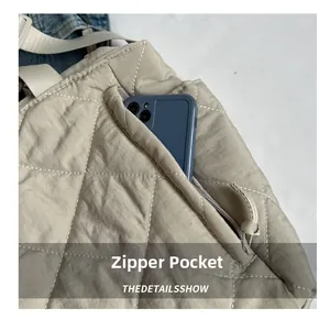 Close-up of side zipper pocket on beige quilted tote bag showing phone storage capacity