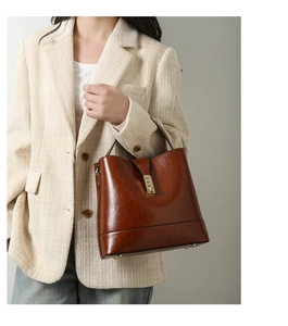 Detail of vintage brown leather handbag with gold buckle held by model in tweed jacket